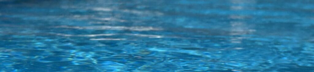 Image shows the blue surface of an outdoor pool reflecting sunlight 
